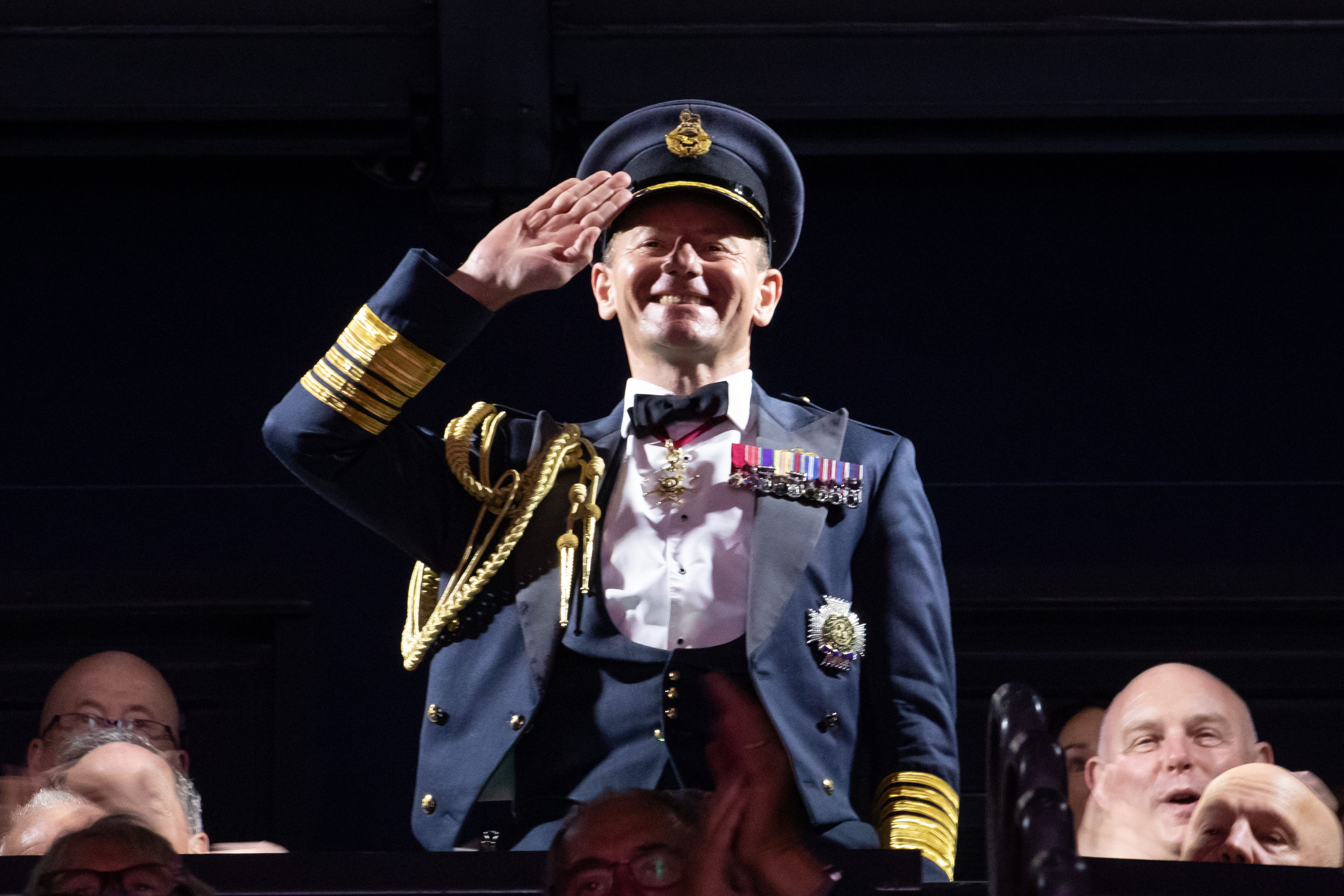 Image shows RAF aviator saluting amid public crowd.